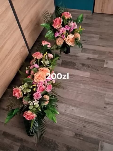 Tall floral arrangement with pink and peach roses, carnations, and greenery in a black vase on wooden flooring