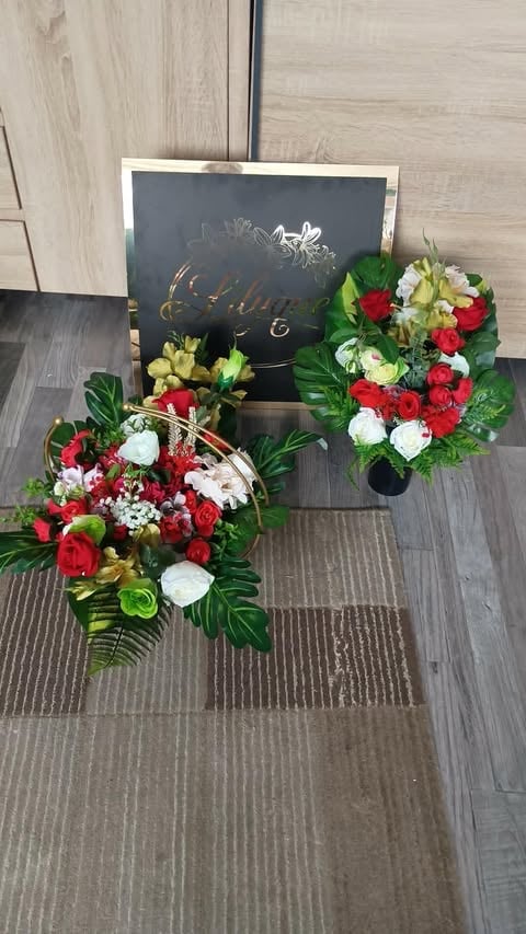 Two red, white, and green floral arrangements displayed on a wooden floor next to a chalkboard sign