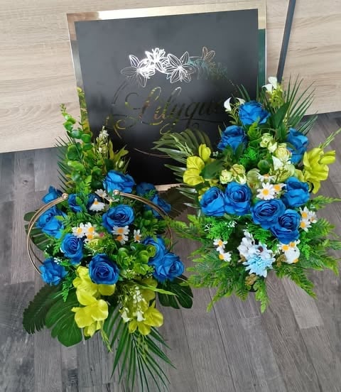 Vibrant floral arrangement with blue roses, yellow flowers, white daisies, and green foliage displayed next to a dark slate chalkboard sign.