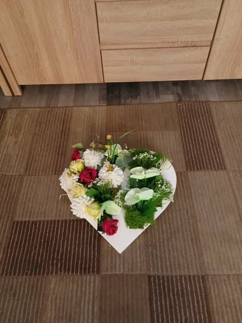 Heart-shaped white floral arrangement with red, white, and yellow flowers on a striped brown tile floor near wooden cabinetry