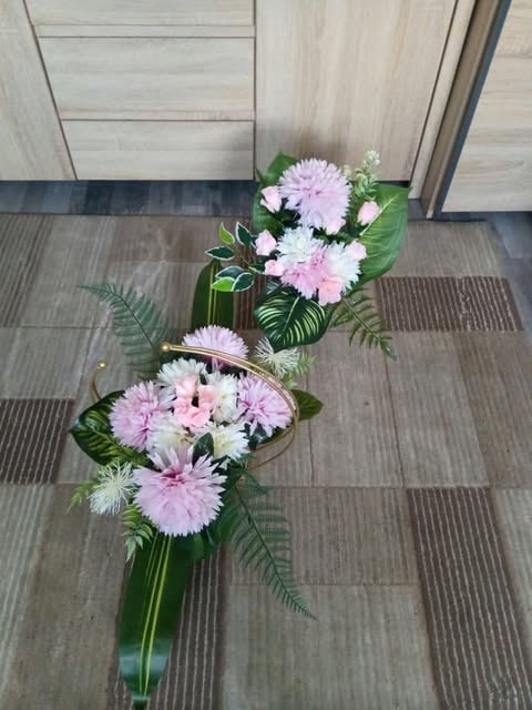 Two floral arrangements with pink and white gerberas and babys breath in glass vases on a striped floor mat near wooden doors