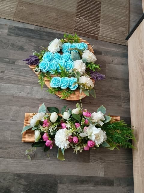 Two floral arrangements on wooden floor: top features blue roses and white flowers, bottom displays pink and white flowers with greenery.