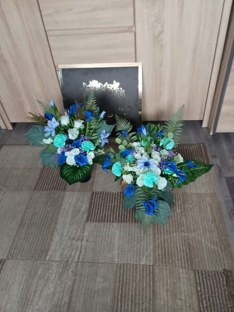 Three floral arrangements with blue, white, and turquoise flowers with greenery on a gray tile floor in front of a dark sign.