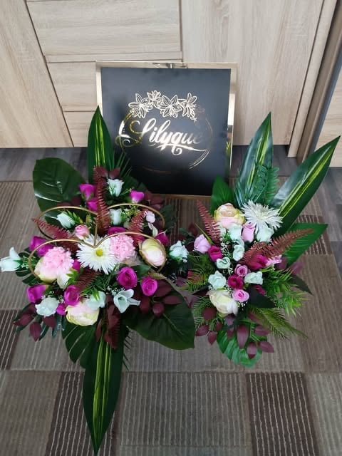 Floral arrangement with pink and white flowers, green foliage, and a black gift box with cursive text on wooden background