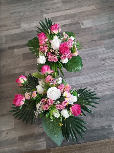 Two-tiered floral arrangement with pink and white flowers, green leaves, displayed on wooden flooring