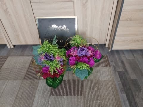 Colorful artificial flowers with green foliage arranged on a striped mat at a doorway entrance