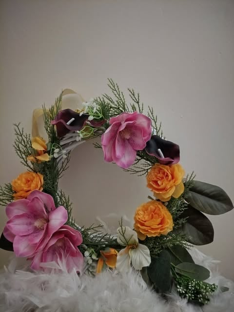 Decorative floral wreath featuring pink, orange, and purple flowers with green foliage and tulle base against neutral background