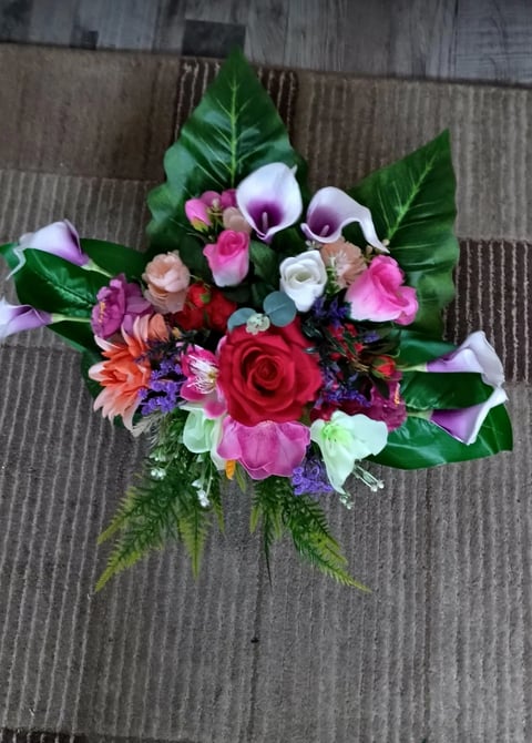 Colorful mixed flower bouquet with red roses, pink peonies, purple calla lilies, and green foliage on a wooden surface