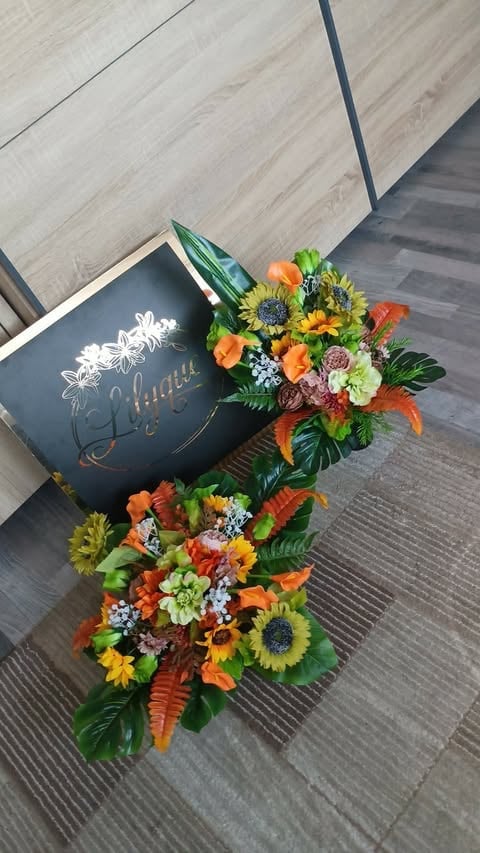 Black hat box with vibrant floral arrangement of sunflowers, orange lilies, and mixed flowers spilling onto wood flooring