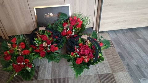 Three vibrant red and pink floral arrangements with greenery displayed on gray floor tile in front of white wall and framed artwork