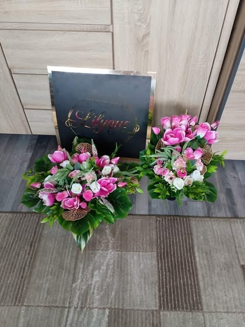 Two pink and white floral arrangements with a dark chalkboard sign displayed on a tiled floor against a wooden wall background
