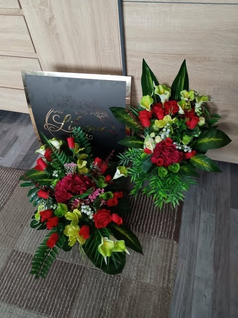 Elegant funeral arrangement with red roses, green chrysanthemums, white babys breath, and dark funeral card on wooden floor.