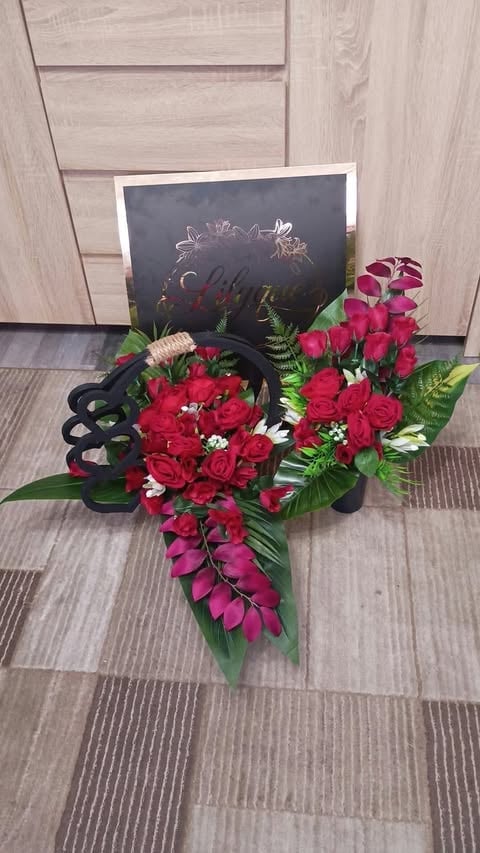 Elegant flower arrangement with red roses and pink orchids in black vase next to chalkboard sign on wooden floor