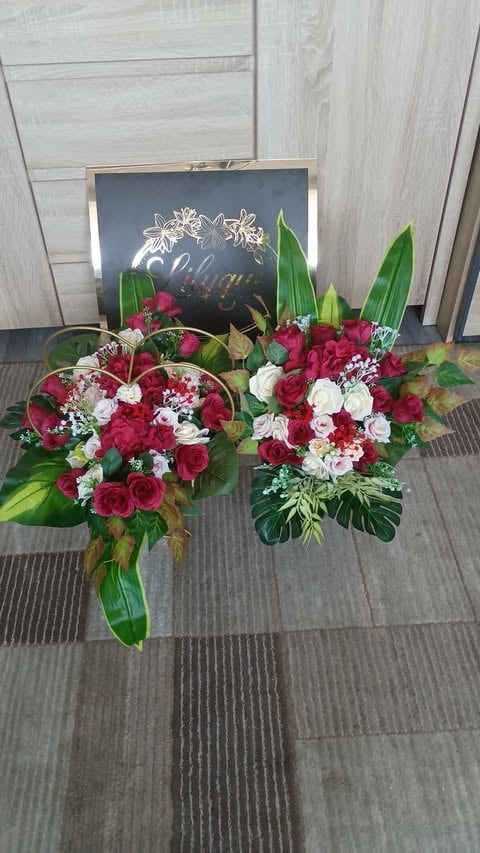 Two vibrant floral arrangements with red and white roses, babys breath, and green foliage displayed on gray tile flooring with a decorative chalkboard sign in the background
