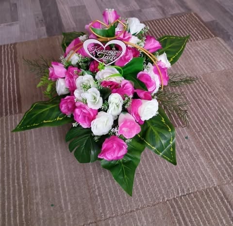 Pink and white flower bouquet with green leaves and a heart-shaped sympathy ribbon on wooden floor