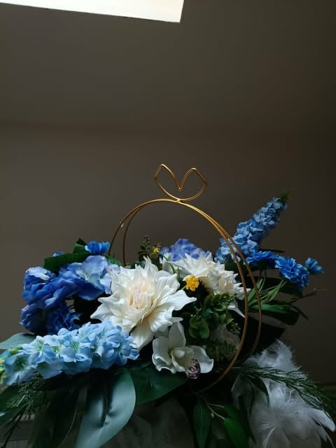Elegant flower arrangement with white peonies, blue hydrangeas, and delphinium in a gold-rimmed circular vase with bow
