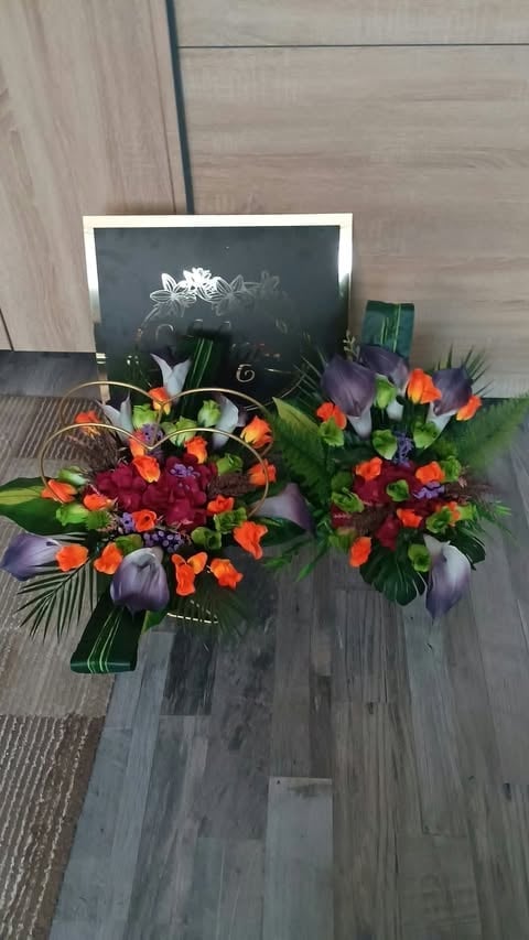Vibrant floral arrangement with orange, red, and purple flowers displayed on wooden flooring next to a chalkboard sign