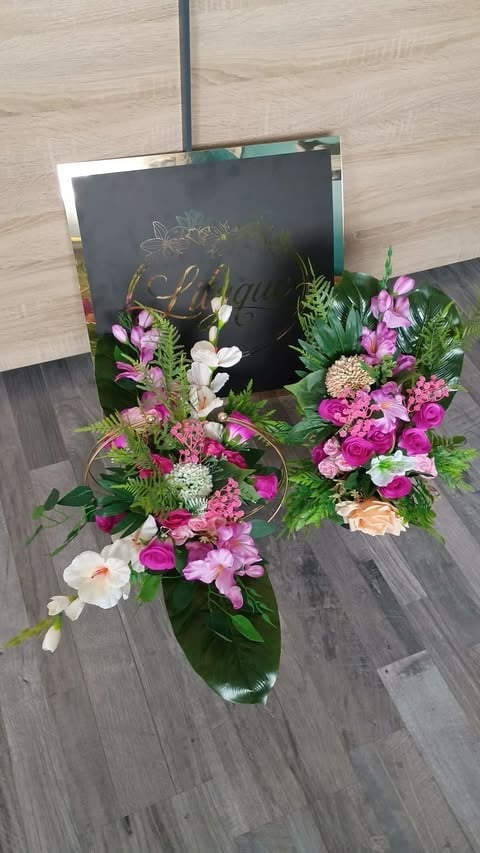 Elegant flower arrangement with pink and white blooms in a green vase, displayed with a dark decorative sign on wooden flooring.