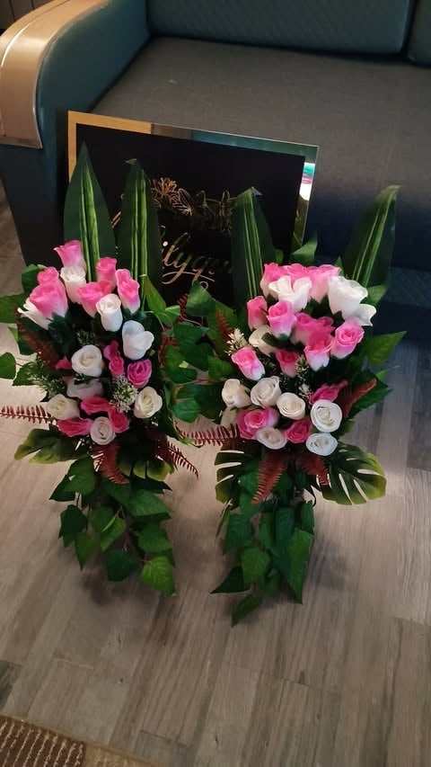 Two floral arrangements with pink and white roses, green foliage, and decorative elements displayed indoors against a teal couch