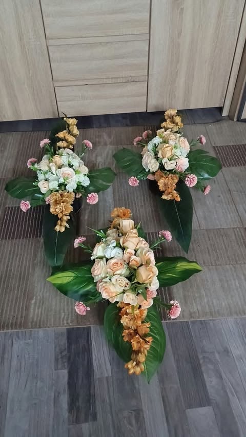 Three tiered floral arrangements with roses, carnations, and golden accents arranged on a dark wood floor indoors