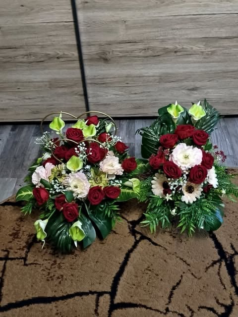 Two floral arrangements with red roses, white flowers, green chrysanthemums, and babys breath on a wooden deck
