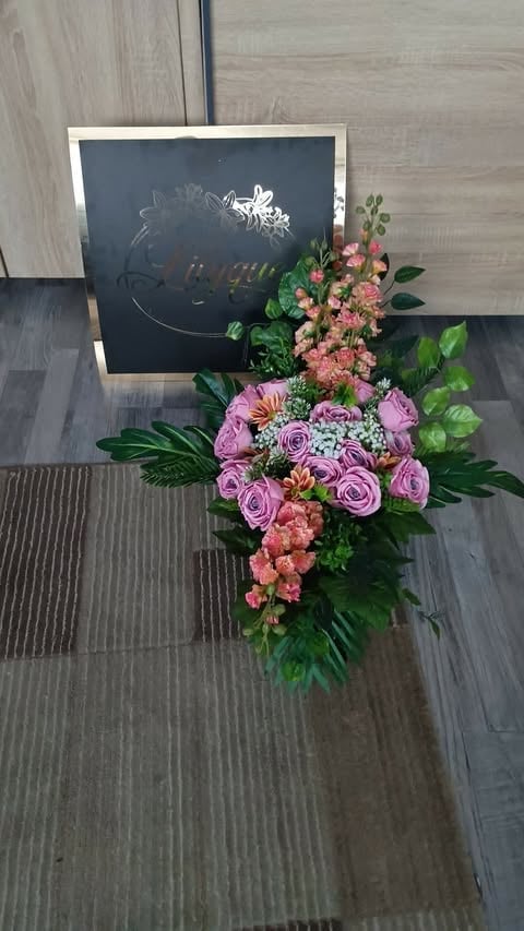 Large floral arrangement with pink and purple roses and coral flowers displayed in front of a black chalkboard sign on wooden flooring
