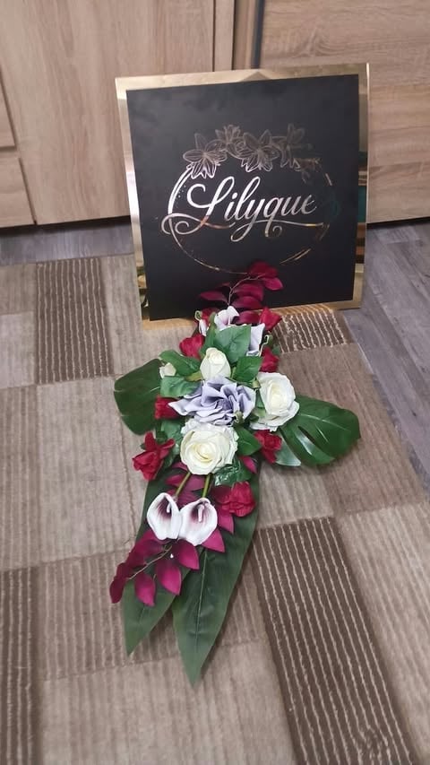Elegant floral arrangement with red roses, white flowers, and purple accents displayed below a black sign with Lilique branding on carpeted floor