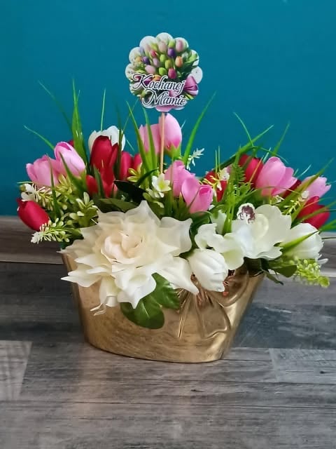 Floral arrangement in gold vase with pink and red tulips, white roses, and greenery with decorative pick, on wooden surface