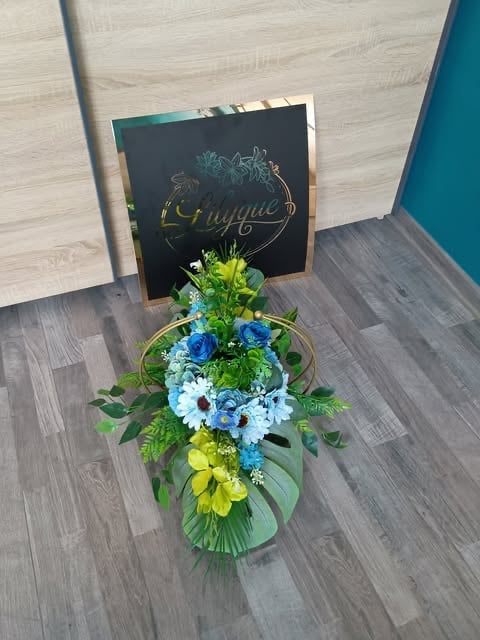 Colorful flower arrangement with blue, white, and yellow blooms in a vase next to a black chalkboard sign on wooden floor