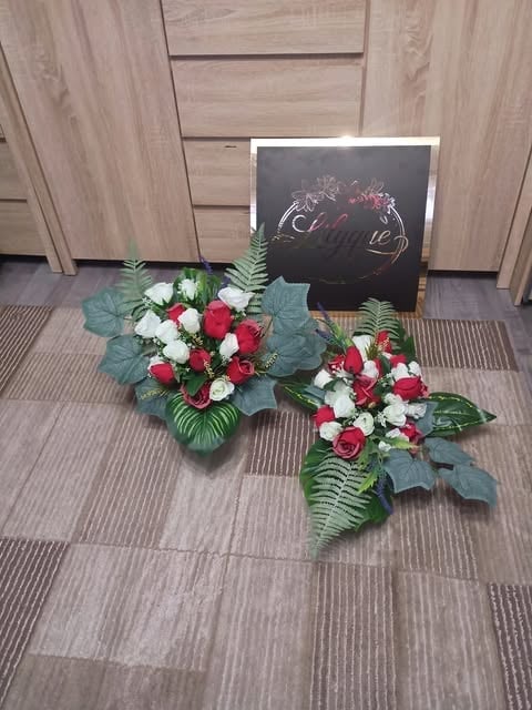 Funeral flower arrangement with red and white roses and ferns beside a dark condolence card on tiled floor