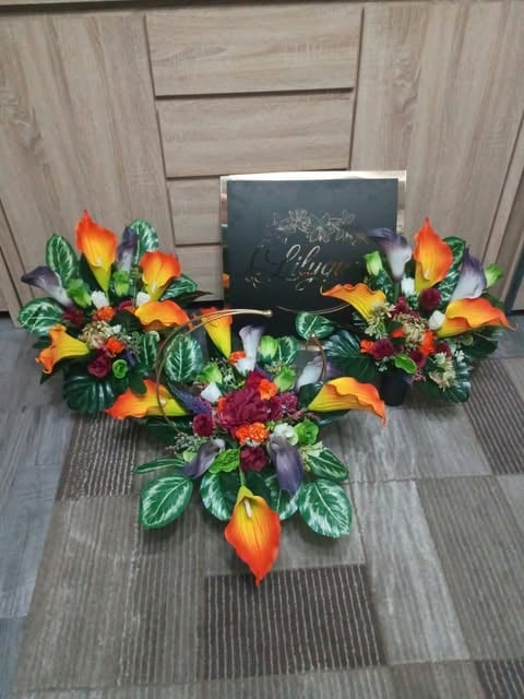 Vibrant tropical floral arrangement with orange calla lilies, burgundy dahlias, and green foliage displayed with a chalkboard sign