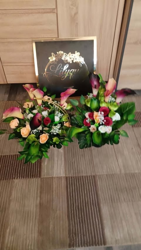 Floral arrangement with colorful roses, calla lilies, and greenery displayed with a black sphere decorated with gold text on wooden flooring