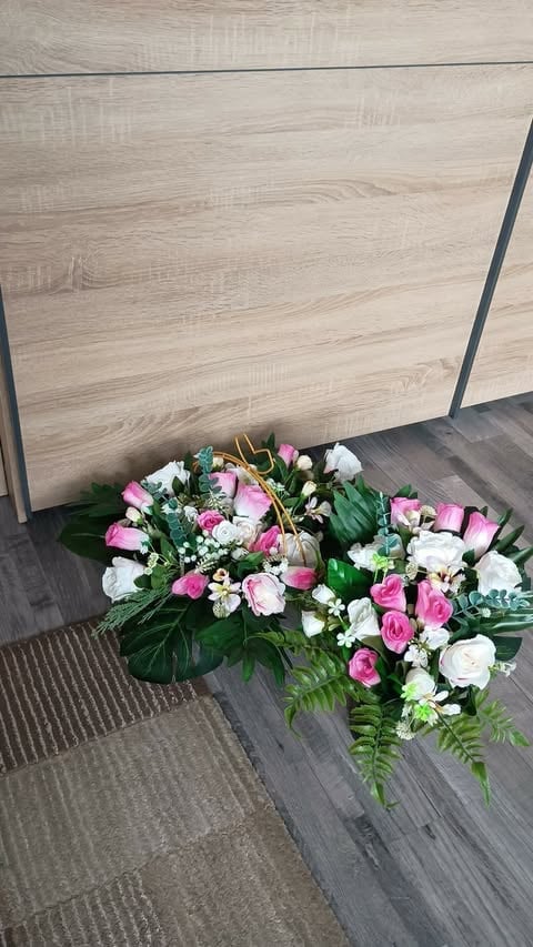 Pink and white floral arrangement with green foliage on dark wood flooring against light wood wall panels