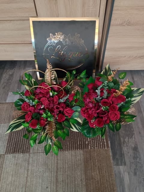 Luxurious floral arrangement with deep red roses, gold accents, and green foliage displayed on wooden floor in front of chalkboard sign