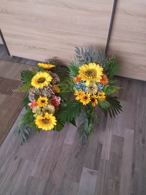 A vibrant flower arrangement with yellow sunflowers, orange and red blooms, and green foliage on a wooden floor indoors