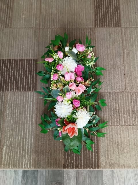Floral casket spray arrangement with pink roses, white chrysanthemums, coral dahlias, and green foliage on striped background