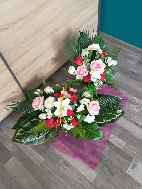 Two tiered floral arrangement with pink roses, white flowers, red blooms, and tropical green leaves on purple mesh base