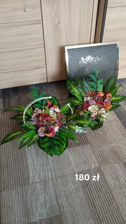 Two floral arrangements with red and white flowers, green foliage, and metal ring handles displayed on gray flooring with wooden wall backdrop, priced at 180 zl