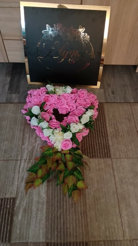 Heart-shaped floral arrangement with pink and white roses, decorative gold frame sign with butterfly artwork on wooden floor