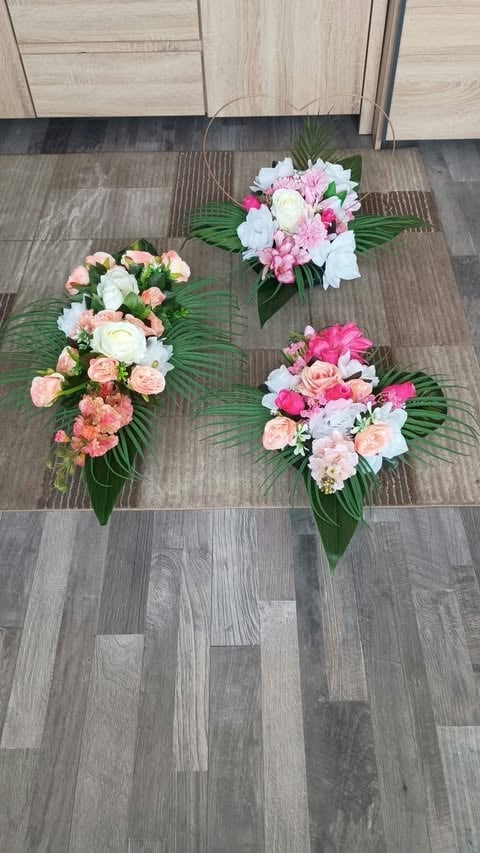 Three floral bouquets arranged on wood flooring, featuring pink, white, and coral roses with green foliage, displayed indoors