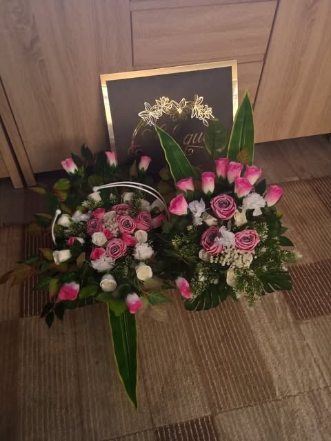 Floral arrangement with pink roses, white flowers, and greenery in a basket beside a chalkboard with gold flowers on wooden floor