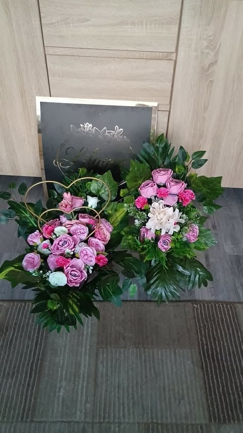 Two floral arrangements with pink roses, white flowers, and greenery displayed on a dark table with a chalkboard sign in the background