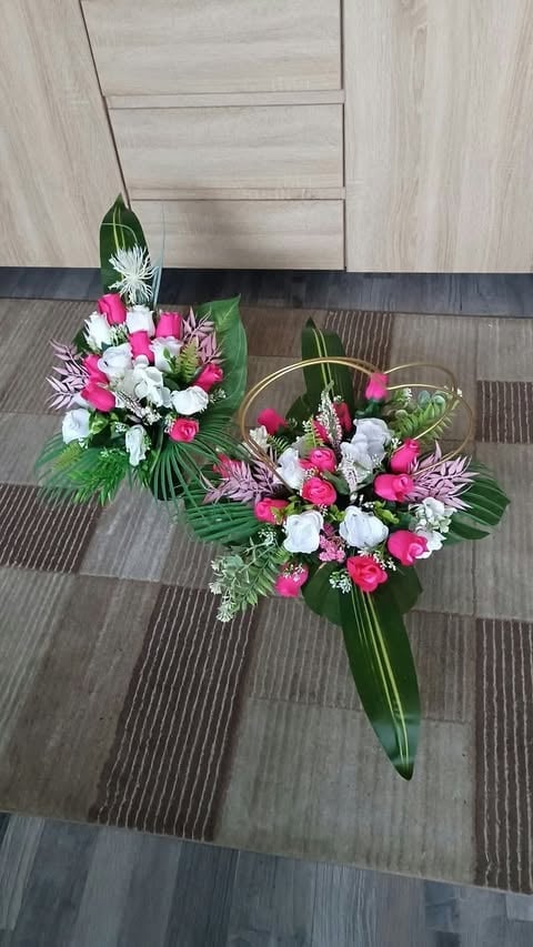 Two floral arrangements with pink roses, white flowers, and green foliage displayed on a wood-textured floor against a light wooden wall.