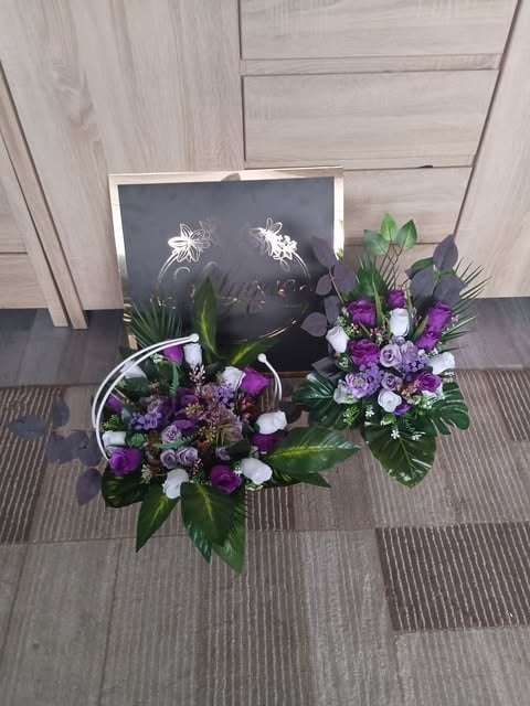 Floral arrangement with purple and white flowers in baskets beside black artwork displayed on light wood paneled wall
