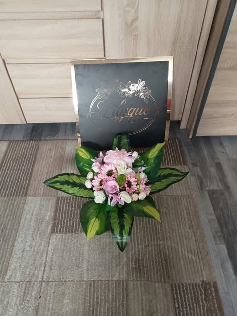 Luxury flower arrangement with pink and white roses and green leaves in a clear vase, displayed with an elegant black branded box.