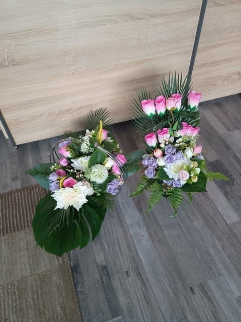 Two vibrant flower arrangements with pink roses, purple flowers, white blooms, and tropical green foliage on a wooden floor
