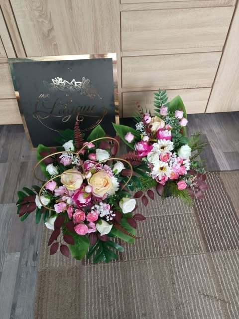 Two heart-shaped flower arrangements with pink, white, and cream roses surrounded by green foliage, displayed with a dark gift bag on wooden flooring
