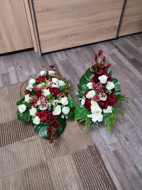 Two floral arrangements with red roses, white flowers, and green foliage displayed on a wooden floor next to cabinetry