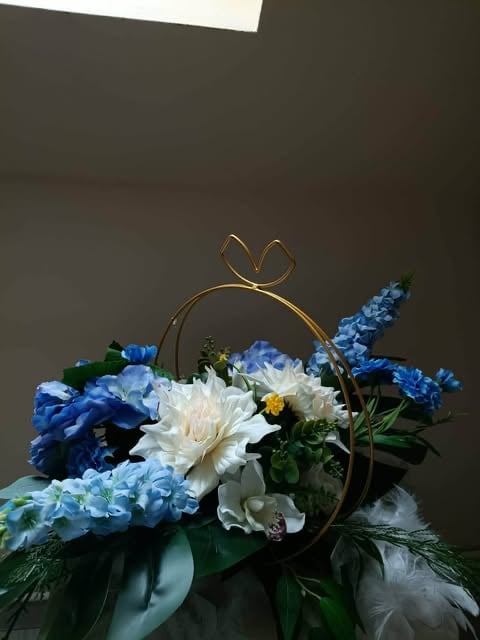 Elegant floral arrangement with white peonies, blue hydrangeas, and delphinium in a decorative gold-rimmed vase with bow detail