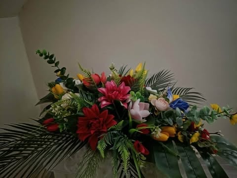 A vibrant flower arrangement featuring red, pink, and yellow blooms with green foliage and tropical leaves against a white background